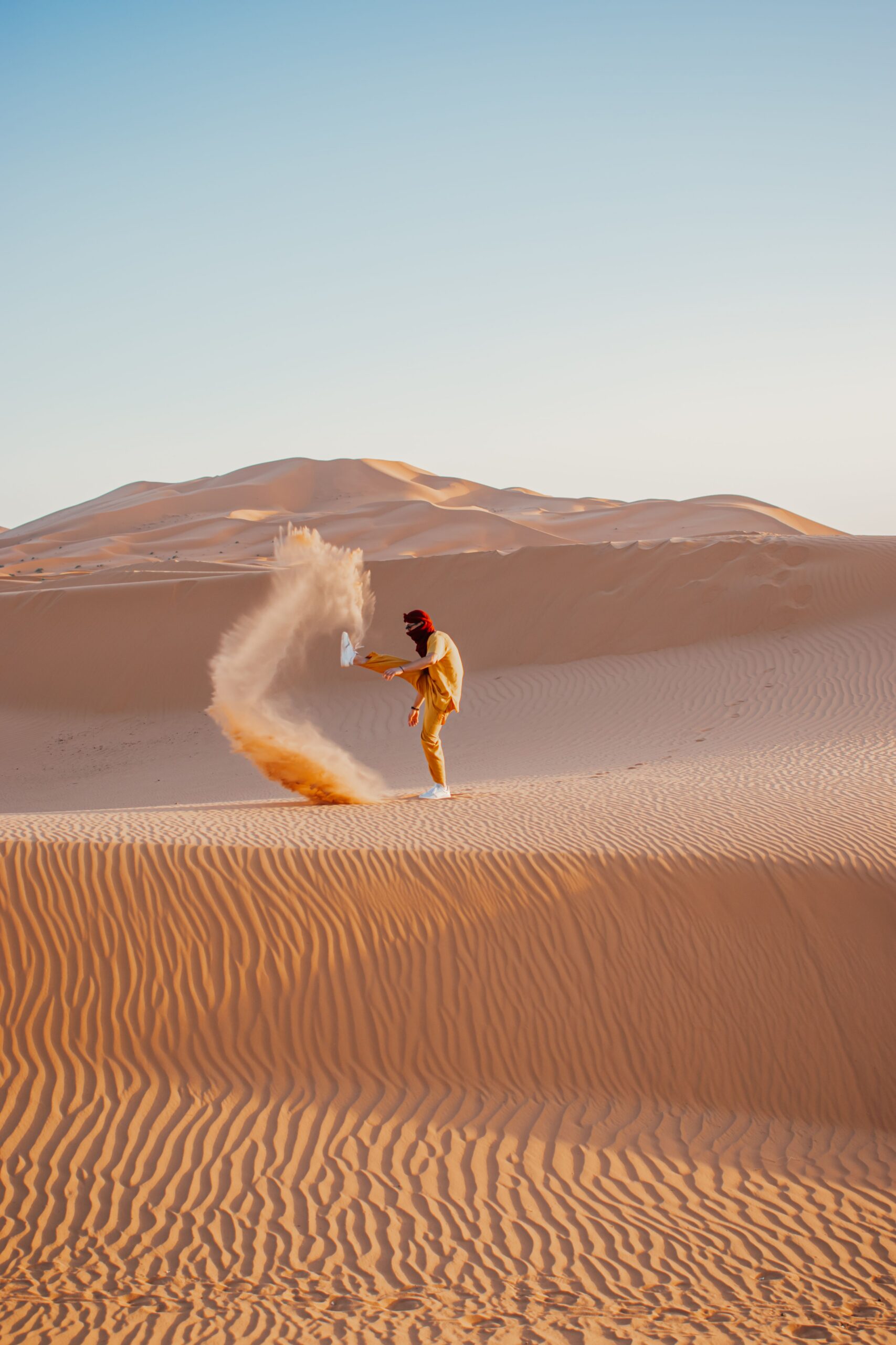 A solitary person kicking sand in Morocco's Merzouga Desert under a clear sky.