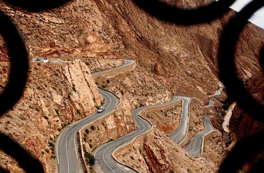 Scenic view of a winding road through the Atlas Mountains framed by ornate ironwork.