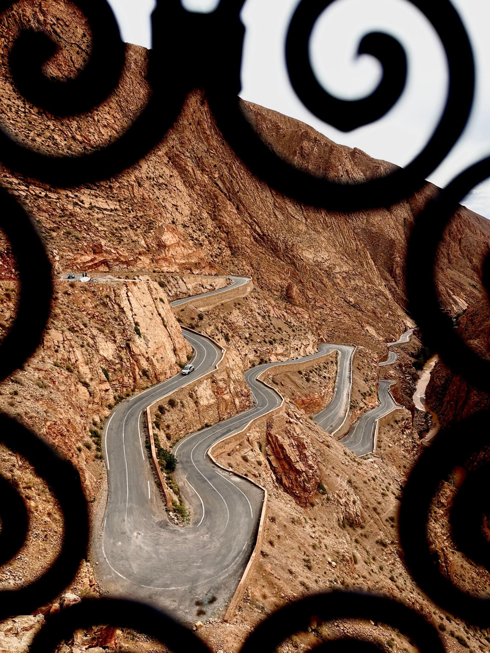 Scenic view of a winding road through the Atlas Mountains framed by ornate ironwork.