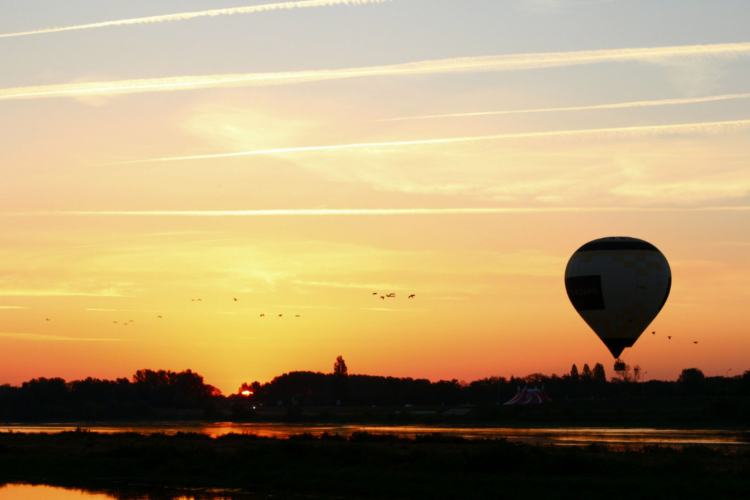 A serene scene of a hot air balloon silhouetted against a vibrant sunset over a river.