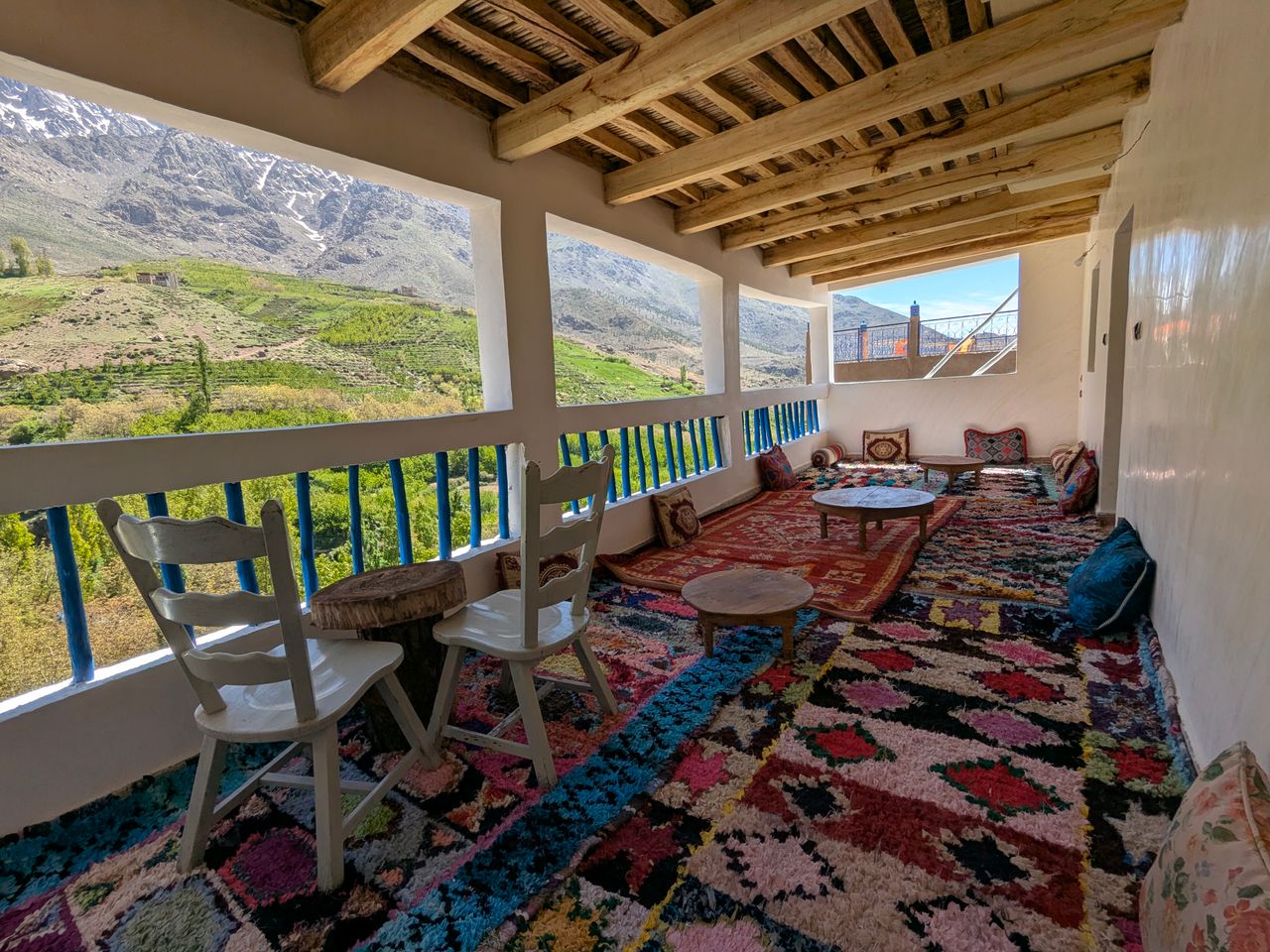 Vibrant Moroccan terrace with mountain view, colorful rugs, and traditional decor.