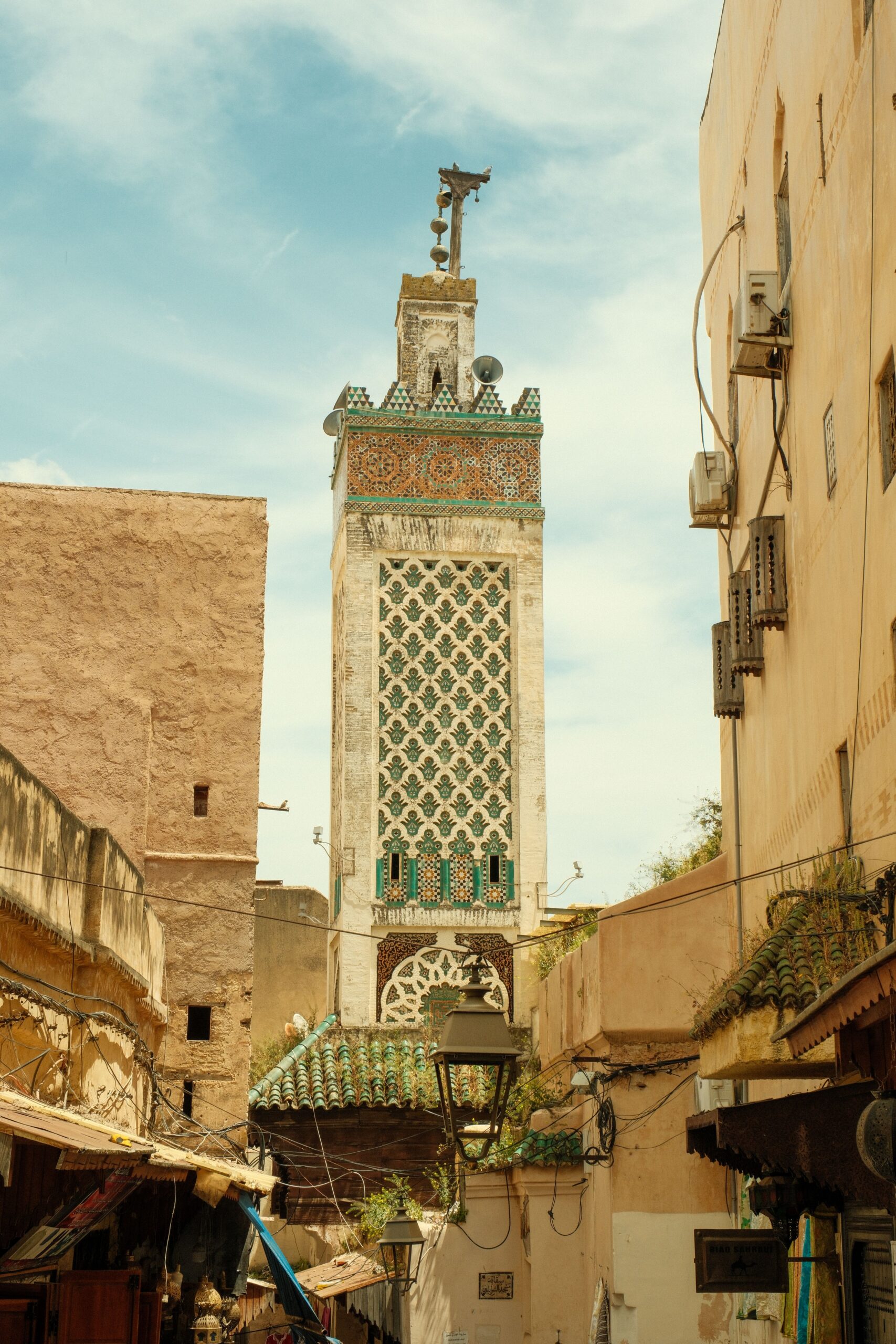 Tall minaret with patterned tiles in historic Fes, Morocco, showcasing traditional Moroccan architecture.