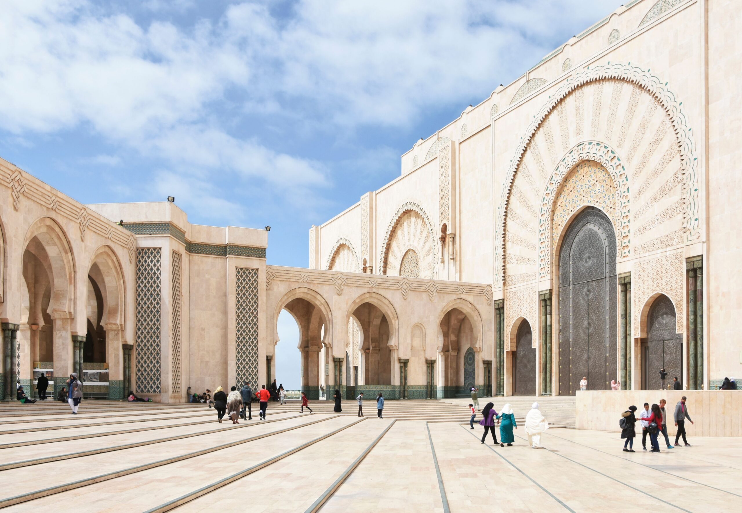 The grand facade of Hassan II Mosque in Casablanca, showcasing Islamic architecture and vibrant outdoor activity.